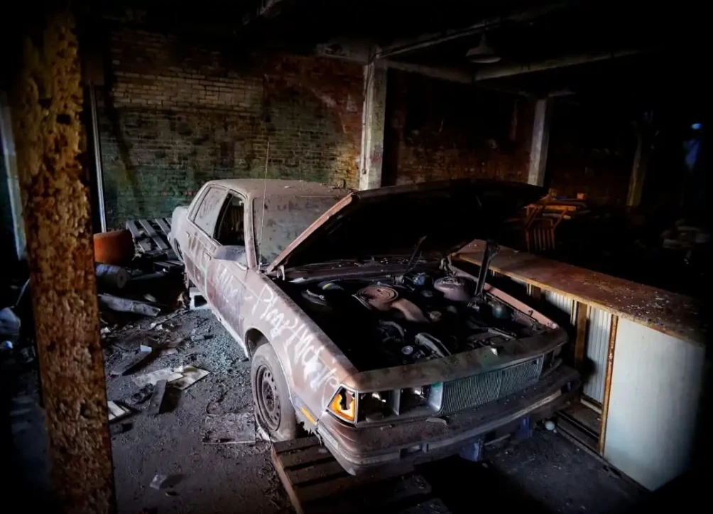 abandoned damaged car with hood open inside a dark garage