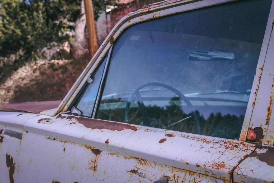 close-up of an old rusted vehicle with peeling paint and corrosion around the window frame